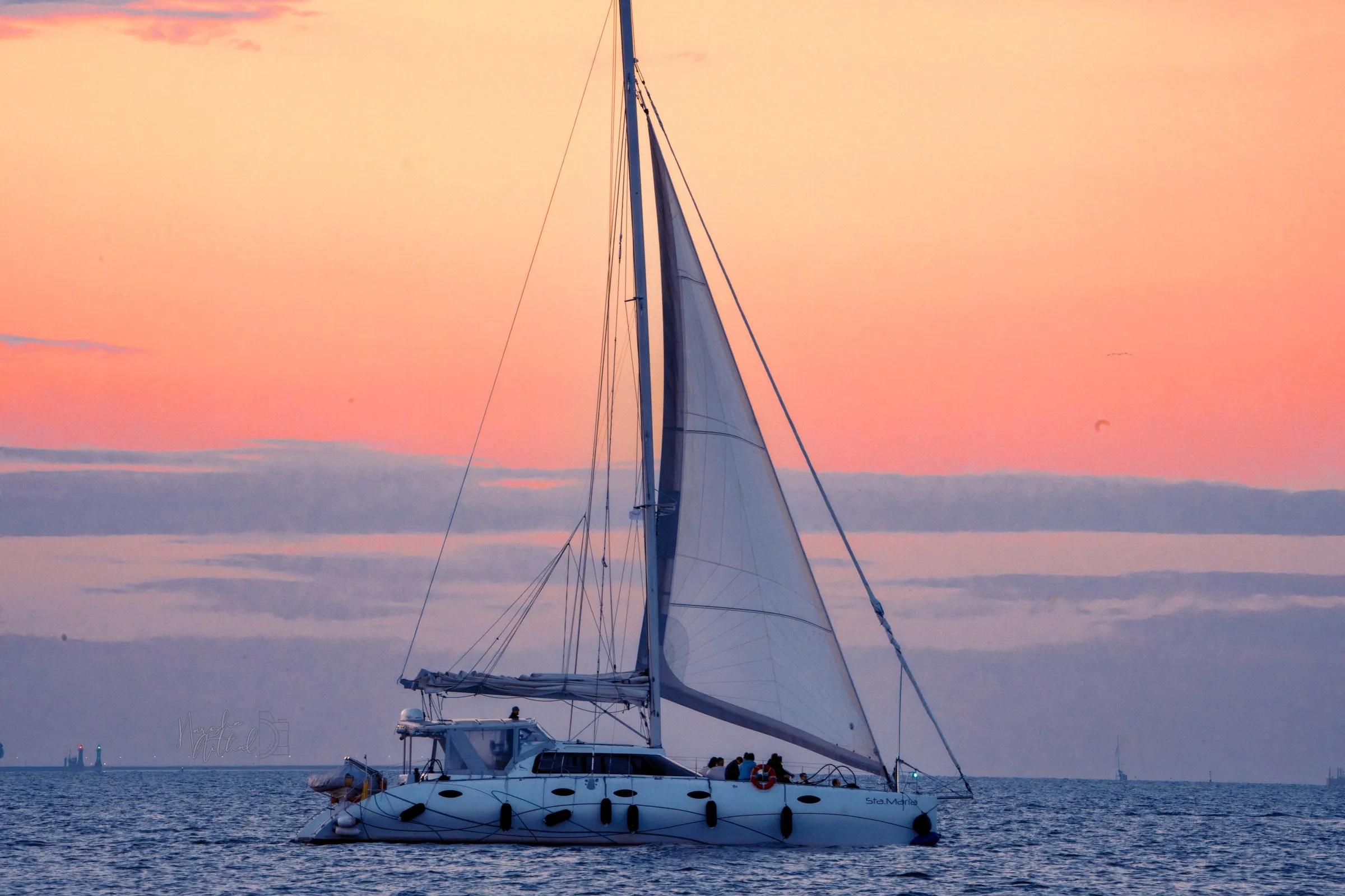 A white sailboat crossing calm water beneath a pink evening sky