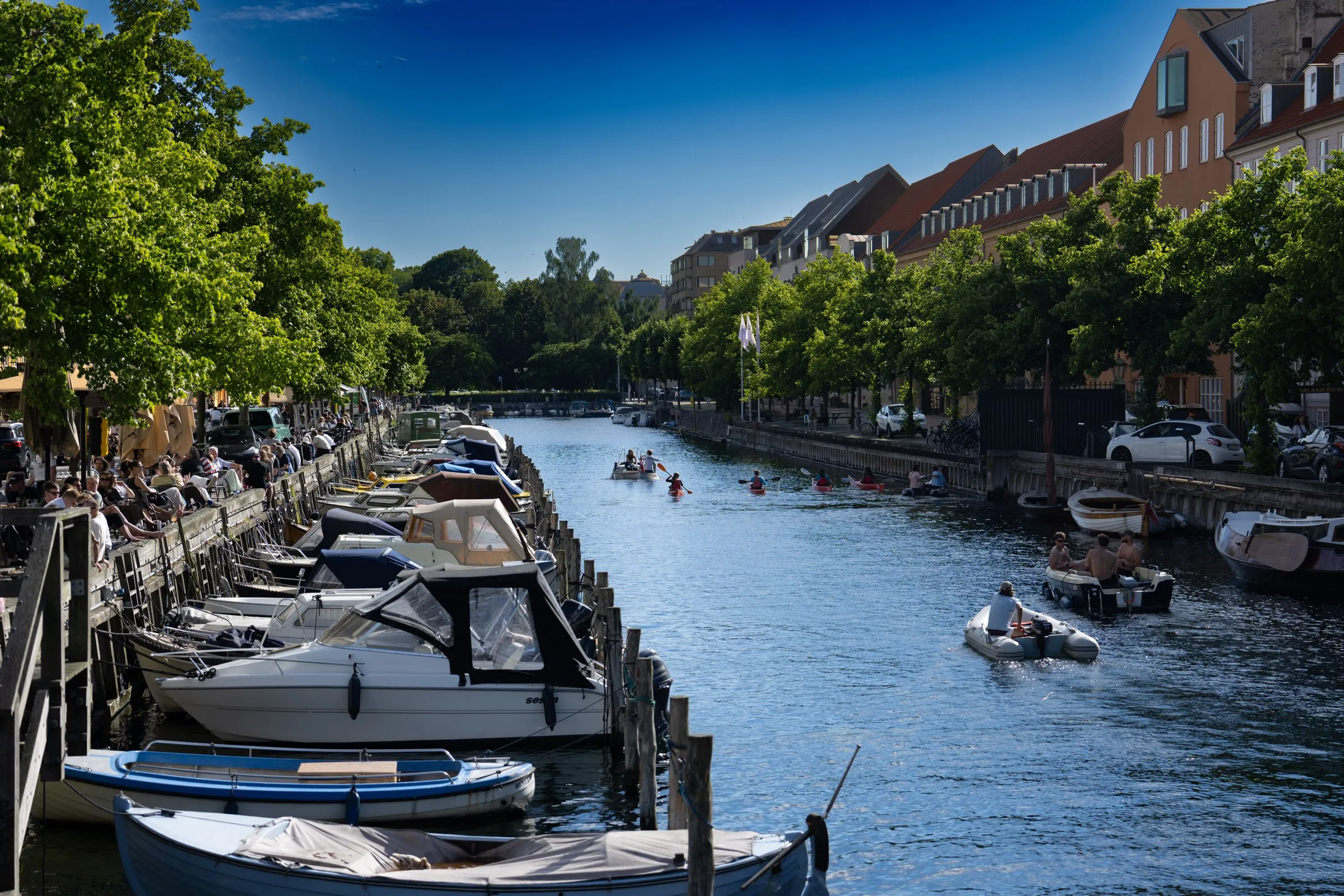 Boats along a tree-lined city canal on a bright day