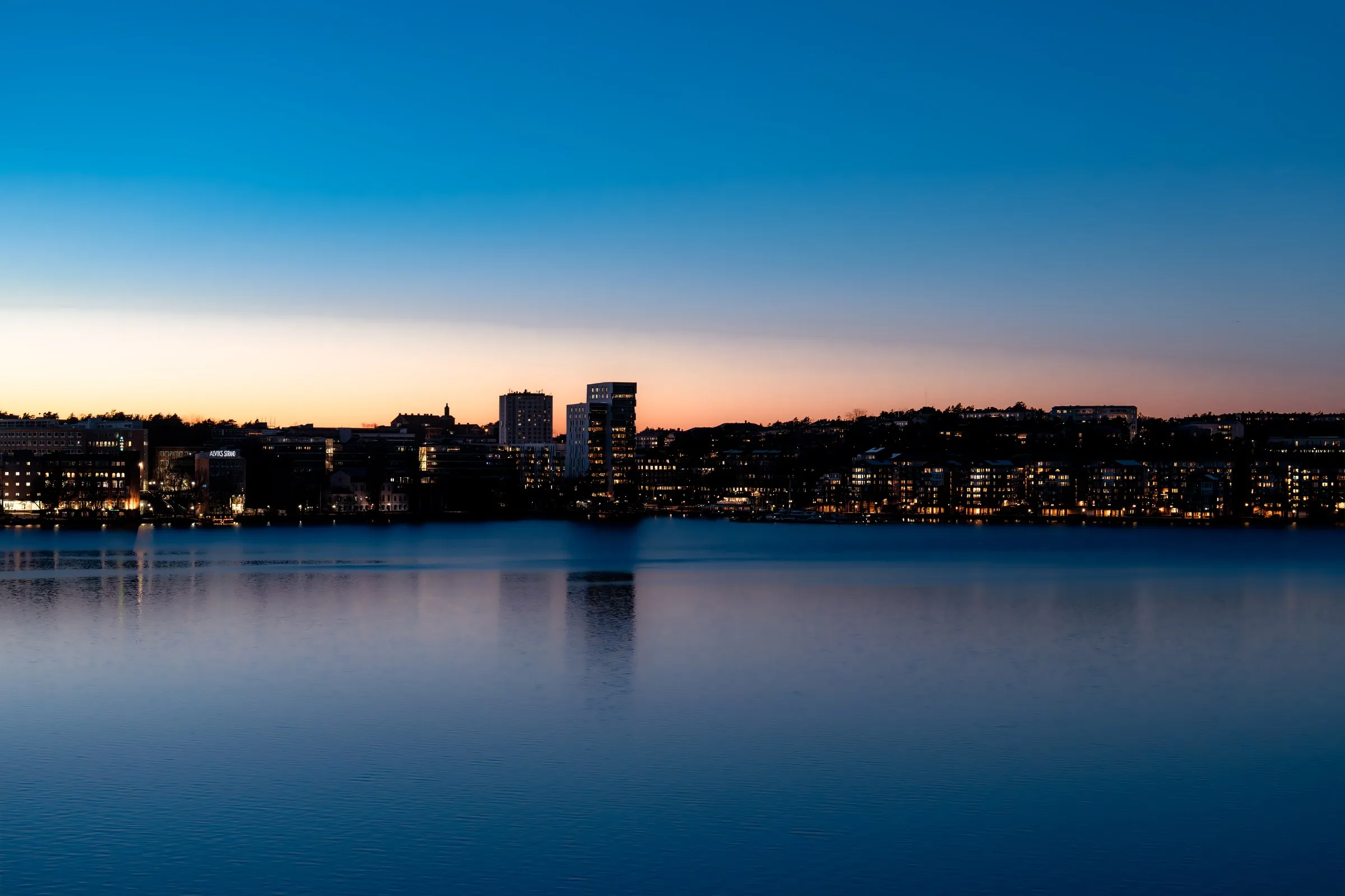 City lights reflected across calm water after sunset